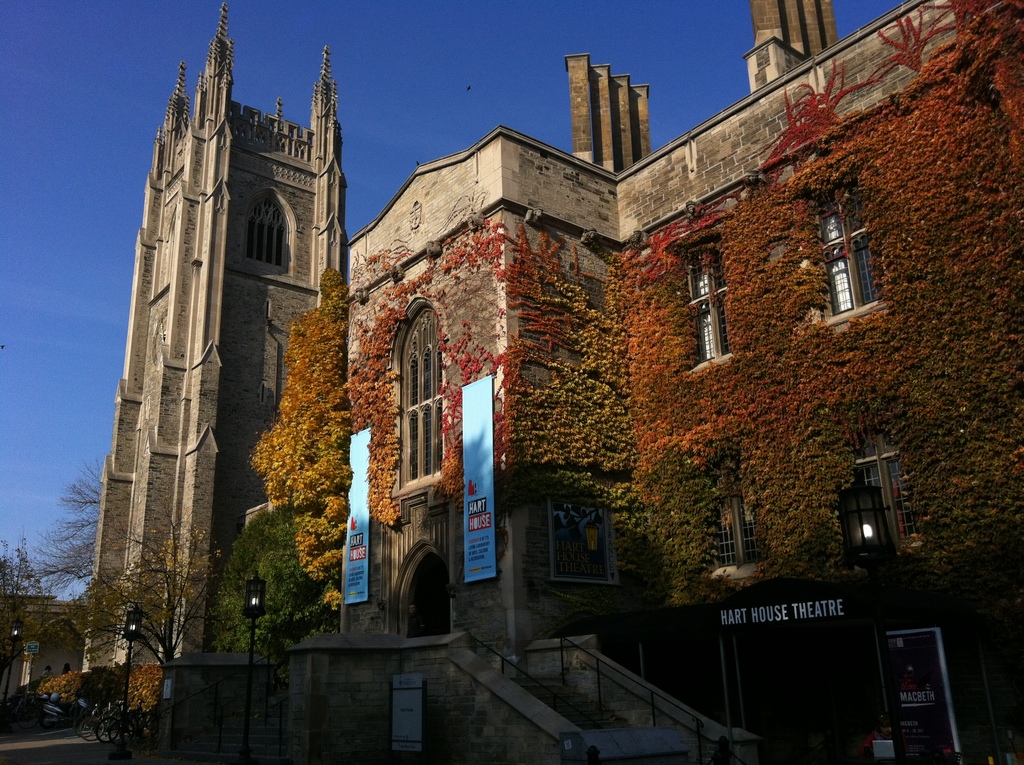 Picture of a building in the Gothic Revival style. It has a short, square tower and is covered in ivy that has coloured red and orange in the fall.